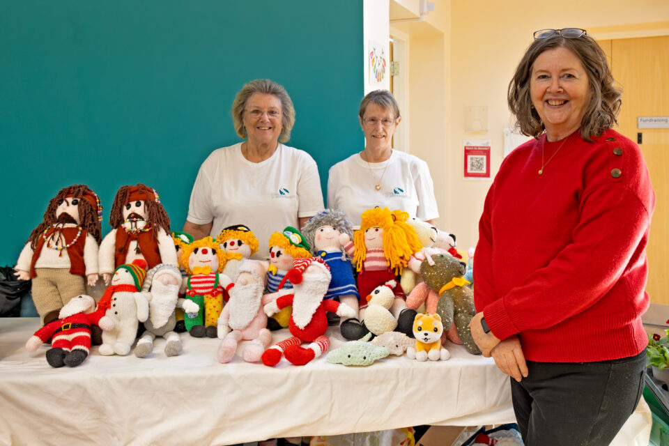 Three women next to knitted and crocheted toys.